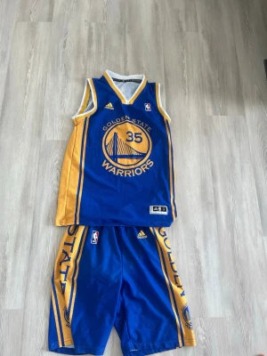 Golden State Warriors basketset - Säljer ett sälsynt blått och gult basketset från Adidas med Golden State Warriors tryck och nummer 35 med spelaren Kevin Durant. Setet består av ett linne och shorts med meshmaterial för bra ventilation. Perfekt för basketträning eller streetstyle.