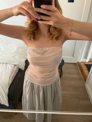 Ljusrosa bandeau tubtopp i mesh - Säljer en ljusrosa bandeau tubtopp i mesh med snygga draperingar på sidorna. Toppen är axelbandslös och har en tight passform som framhäver midjan. Perfekt för dig som vill ha en enkel men trendig topp till sommaren.