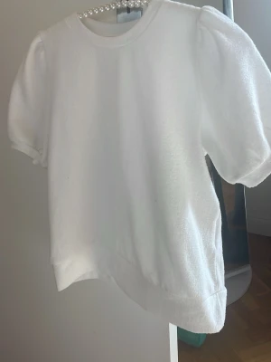 Vit puffärmad topp i frotté - Säljer en vit topp med puffärmar och rund halsringning. Toppen är gjord i mjuk frotté och har korta ärmar med lätt resår vid ärmslutet. Perfekt för en fräsch och enkel look.