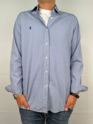 Ralph lauren skjorta randig M - Supersnygg randig ralph lauren skjorta. Size 15 1/2 som motsvarar M. Bredd: 45cm. Längd 70cm! Modellen är 180. Rekomenderad längd: 180-186cm. Fint skick, reva bak på skjortan. Hör av dig vid intresse 🤩