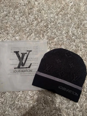 Svart mössa  - Snygg svart mössa  med diskret monogrammönster och grå rand längst ner. Mössan har en tight passform och är tillverkad i ett mjukt, stretchigt material som känns bekvämt på huvudet. Perfekt accessoar för att lyfta din outfit.