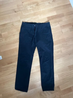 Svarta chinos med raka ben - Snygga svarta chinos med klassisk rak passform och diskreta sidofickor. Byxorna har bälteshällor, knappgylf och två bakfickor med knapp. Tillverkade i ett mjukt bomullstyg som ger en clean look.