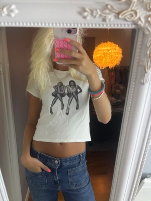 Vit croppad t-shirt med tryck - Säljer en vit croppad t-shirt med coolt svart tryck av två personer i futuristiska outfits på framsidan. T-shirten har korta ärmar och en avslappnad passform. Perfekt för dig som vill ha en unik och trendig look.