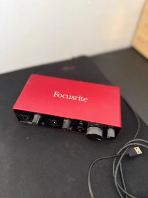 Focusrite Scarlett 2i2 ljudkort 3rd generation - Rött USB-ljudkort från Focusrite, modell Scarlett 2i2. Metallchassi med flera reglage och anslutningar på framsidan för mikrofon och instrument. Perfekt för hemmastudio eller streaming. Kompakt och stilren design med tydliga kontroller.