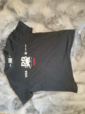 Hugo boss Svart Red Bull Racing t-shirt - Säljer en svart Hugo boss t-shirt med Red Bull Racing-tryck och loggor från Visa, Cash App och Hugo. T-shirten har rund hals och korta ärmar. Perfekt för dig som gillar motorsport och vill ha en sportig look.