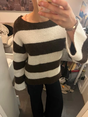 Brun och vit randig stickad tröja - Stickad tröja med breda bruna och vita ränder. Tröjan har en lös passform, rund halsringning och långa ärmar med lätt utsvängda ärmslut. Materialet ser mjukt och fluffigt ut, perfekt för kyligare dagar. Enkelt och trendigt plagg att styla till jeans eller kjol.