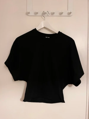 Svart croppad t-shirt - En svart croppad t-shirt med lös passform och korta ärmar. Perfekt till jeans eller kjol för en avslappnad och trendig look. Tillverkad i mjuk bomull som känns skön mot huden.
