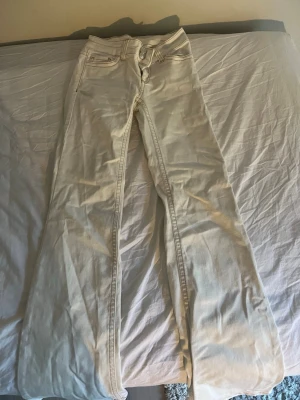 Vita bootcut jeans med kontrastsömmar - Säljer ett par vita bootcut jeans med snygga kontrastsömmar och klassiska fem fickor. Jeansen har utsvängda ben och detaljerade bakfickor med broderade mönster.  I storlek 32🥰