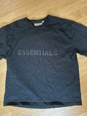 Svart Essentials t-shirt med tryck - Snygg svart t-shirt från Essentials med stort tryck på bröstet. Klassisk rund halsringning och korta ärmar. Perfekt för en avslappnad och trendig stil.