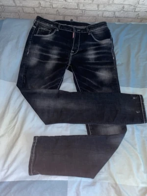 Svarta Dsquared2 jeans med slitningar - Säljer ett par svarta jeans från Dsquared2 med coola slitningar och tvättade detaljer. Klassisk femficksmodell med vita kontrastsömmar och röd logotagg vid gylfen. Perfekta för dig som gillar streetwear och vill sticka ut lite extra. SKINNY!!