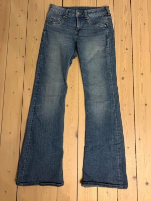 Blå utsvängda jeans från H&M - Blå jeans från H&M med utsvängda ben och klassisk femficksmodell. Jeansen har en lätt tvättad look och är tillverkade i denim med en skön passform. 