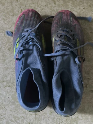 Blå adidas f50fotbollsskor med neonränder - Säljer ett par blå adidas f50 fotbollsskor med högt skaft och snörning. Skorna har neonfärgade detaljer i gult och rosa längs sidorna och framtill. Ovandelen är i textilmaterial med en modern, strömlinjeformad design som passar perfekt för spel på planen.Jag kan tvätta skorna