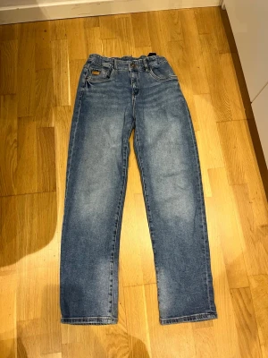 Blå raka jeans från lab industries  - Säljer ett par klassiska blå jeans från Lee med rak passform och hög midja. Jeansen har fem fickor, bälteshällor och Lee-lapp bak i midjan. Tillverkade i slitstark denim med snygg tvätt och subtila slitningar. Perfekta till en avslappnad look.