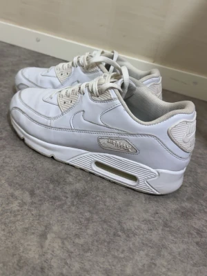 Nike Air Max 90 vita sneakers - Säljer ett par klassiska Nike Air Max 90 sneakers i helvitt. Skorna har en chunky sula med synlig Air Max-dämpning, snörning och detaljer i vitt läder och syntet. Perfekta för dig som gillar en clean och sportig look.