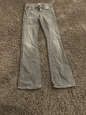 Grå bootcut jeans med låg midja - Snygga grå jeans med bootcut passform och låg midja. Klassisk femficksmodell med dragkedja och knapp framtill. Perfekta för dig som gillar en avslappnad och trendig stil. Materialet är denim i bomull.