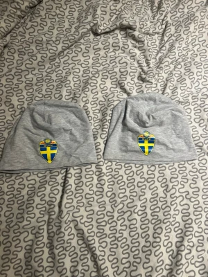 Grå mössa med Sverige-emblem - Säljer en grå mössa i mjukt tyg med Sveriges landslagsemblem framtill. Perfekt för dig som vill visa ditt stöd för Sverige och hålla dig varm. Enkel och stilren design med broderad detalj i blått och gult.