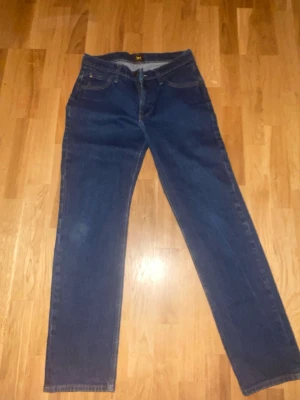 Blå raka jeans från Lee - Snygga blå jeans från Lee i rak modell, tillverkade i ekologisk bomull. Klassisk femficksdesign med gylf och knapp framtill. Perfekta för en avslappnad och stilren look. Möts endast i stockholm 