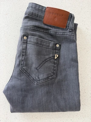 Grå jeans från Dondup Monroe - Snygga grå jeans från Dondup, modell Monroe. Jeansen har klassisk femficksdesign, silverfärgade nitar och en liten D-detalj på fickan. Tillverkade i Italien och har en skön tvättad look som passar till allt. W27 L32 