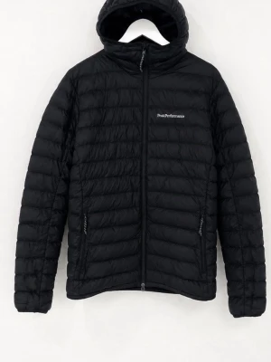 Svart dunjacka Peak Performance - Snygg svart dunjacka från Peak Performance med huva och dragkedja framtill. Jackan har två sidofickor med dragkedja och diskret logga på bröstet. Lättviktigt material och quiltad design som håller värmen under kalla vinterdagar men även skön till våren och höst!!!!!                                      KÖPT FÖR 2200 PÅ STADIUM