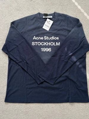Blå långärmad t-shirt Acne Studios - Snygg marinblå långärmad t-shirt från Acne Studios med vit text 'Acne Studios STOCKHOLM 1996' på bröstet. Priset går att diskutera. Passar dig som är 175-185 cm.