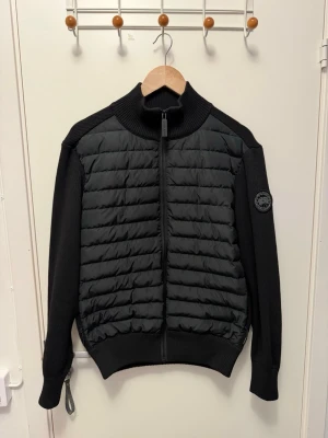 Svart canda cardiganjacka black label  - Snygg svart cardiganjacka med quiltad framsida och stickade ärmar samt rygg. Jackan har hög krage, hel dragkedja och en patch på ärmen. Perfekt för lager-på-lager och streetstyle.