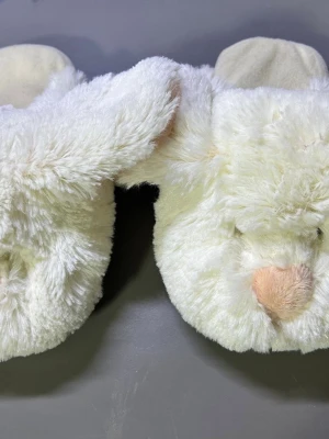 Vita fluffiga kanintofflor - Supersöta vita tofflor i form av kaniner med mjuk pälsimitation och rosa nos. Tofflorna har halkskydd under sulan och detaljer som öron och broderade ansikten. Perfekta för att hålla fötterna varma och ge en gullig touch hemma. Kolla måtten för Stlk 