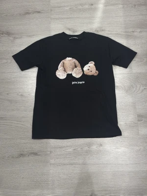 Svart Palm Angels t-shirt med björntryck - Svart t-shirt från Palm Angels med ikoniskt tryck av en nallebjörn utan huvud på bröstet och texten 'Palm Angels' under. Klassisk passform och rund hals. Perfekt för dig som gillar streetwear och vill sticka ut med en unik design.