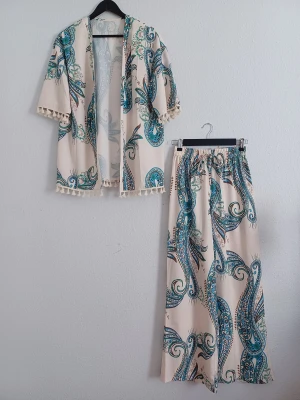 Kimono & Wide-leg pants set - Colorful two-piece set featuring a tropical flowing peacock-print kimono blouse with pom-pom trim and relaxed wide-leg pants. Lightweight, non-stretch and non-transparent fabric with a comfortable, flowy fit.  Size: XS / 34 Condition: Very good — worn once for a themed event. Colour: Tropical peacock print Material: Polyester  Measurements: • Blouse length: 75 cm • Sleeve: 27 cm • Pants length: 105 cm  Perfect for vacations, beach days, brunch dates, evenings out or everyday chic.