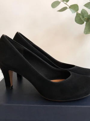 Clarks svarta pumps skinn & mocka – stl 39 - 🖤 Klassiska svarta pumps från Clarks i skinn och mocka. Tidlös modell med rundad tå och ca 7,5 cm klack.  🔖 Stl 39  📏 Innersula ca 25 cm Klackhöjd ca 7,5 cm  🧵 Skinn och mocka  ✨ Fint skick med normala bruksspår. Visst slitage finns på inner- och yttersulor. Se bilderna för egen bedömning av skicket.