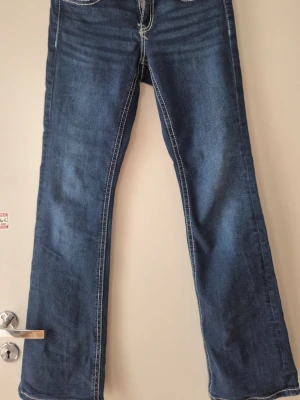 Blå bootcut jeans från Gina Tricot - Säljer ett par klassiska blå bootcut jeans från Gina Tricot. Jeansen har kontrastsömmar, fem fickor och en snygg utsvängd passform. Perfekta till sneakers eller boots och gjorda i mjuk bomull med lite stretch.