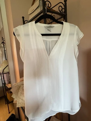 Vit blus från H&M Conscious - Snygg vit blus från H&M Conscious med v-ringning och diskreta veck framtill. Blusen har korta ärmar och är tillverkad i ett lätt, luftigt material som passar perfekt till sommaren. Enkel och stilren design som är lätt att matcha.