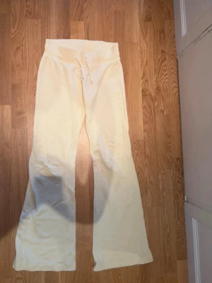 Gula mjukisbyxor med dragsko - Snygga ljusgula mjukisbyxor med bred mudd i midjan och dragsko för skön passform. Byxorna har utsvängda ben och är gjorda i ett mjukt, bekvämt material som passar perfekt för chill dagar. Enkel och stilren design utan synligt märke.