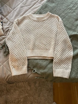 Beige stickad tröja från H&M - Säljer en beige stickad tröja från H&M med hålmönster och croppad passform. Tröjan har långa ärmar, ribbade muddar och rund halsringning. Perfekt för lager på lager och ger en trendig look till din outfit.