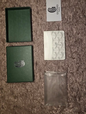 Vit plånbok - Säljer ett stilrent vitt kortfodral med det klassiska mönstret och loggan på framsidan. Fodralet har flera fack för kort och är tillverkat i läder med canvasdetaljer. Perfekt för dig som vill ha något exklusivt och snyggt i fickan.