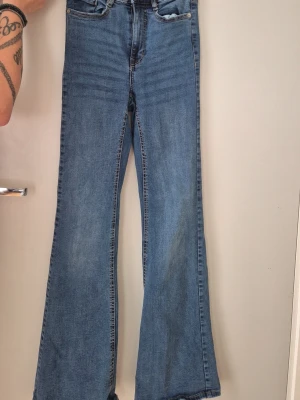 Blå bootcut jeans med hög midja - Säljer ett par klassiska blå bootcut jeans med hög midja och femficksmodell. Jeansen har utsvängda ben och är tillverkade i ett mjukt denimtyg. Perfekta för dig som gillar retrostil och vill ha ett par bekväma jeans med snygg passform. Inköpta på Bubbleroom. 