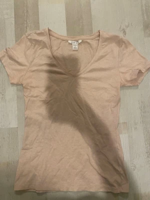 Ljusbeige v-ringad t-shirt - En enkel och stilren ljusbeige t-shirt med v-ringning och korta ärmar. Tillverkad i mjuk bomull som känns skön mot huden. Perfekt basplagg att matcha med allt i garderoben.