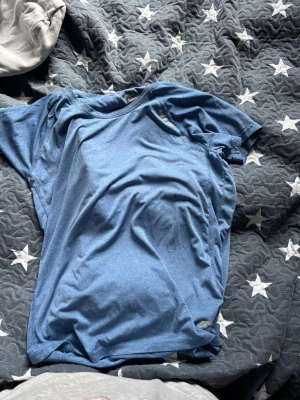 Blå t-shirt från Karhu i bomull - Säljer en blå t-shirt från Karhu i storlek XL. T-shirten har en klassisk rund halsringning och korta ärmar. Materialet är mjukt och skönt, perfekt för en avslappnad stil. Enkel och stilren design utan tryck eller mönster.