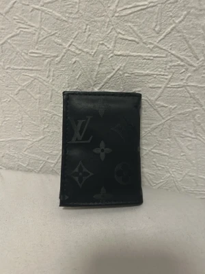 Plånbok - Snygg svart plånbok i läder med det klassiska monogrammönstret. Plånboken har flera kortfack, ett fönster för ID och en knappstängning. Perfekt storlek för fickan och stilren design som passar till allt. Aldrig använd och är i ny skick och inga skador .