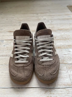 Adidas Spezial bruna sneakers - Säljer ett par Adidas Spezial sneakers i brunt mocka med beigea detaljer och klassiska tre ränder på sidan. Skorna har vita snören och gummisula för en retro look. Perfekta för dig som gillar streetwear och vill ha något unikt i garderoben.