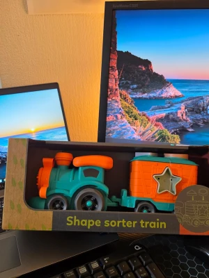 Färgglatt sorteringståg i bio-plast(Robetoy.se) - Säljer ett lekfullt sorteringståg i plast med starka färger som turkos, orange och grönt. Tåget har hjul och en vagn med stjärnformad öppning för att sortera olika former. Perfekt för yngre barn som gillar att leka och lära sig former.