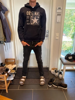 Marin blå hoodie med tryck och huva - Säljer en svart hoodie med stor vit text 'ORIGINAL' och stjärntryck på bröstet. Hoodien har klassisk känguruficka framtill och justerbar huva. Perfekt för dig som gillar en avslappnad och cool stil.