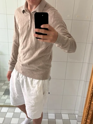 Beige stickad tröja från Filippa K - Snygg beige stickad tröja från Filippa K med klassisk krage och knappar vid halsen. Tröjan har långa ärmar och ribbade muddar vid ärmslut och nederkant. Perfekt till både jeans och chinos för en clean look.