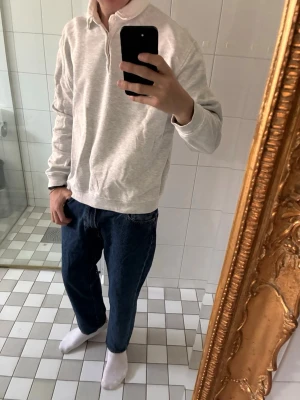 Polo topp från Zara - En stilren ljusgrå långärmad polotopp med krage och knappar framtill. Toppen har en relaxed passform och är tillverkad i mjukt bomullsmaterial. Perfekt för en clean och enkel look.