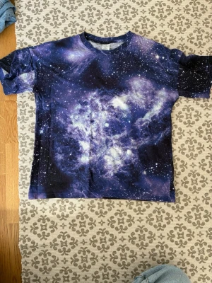 Galaxy t-shirt med rymdmönster - Cool t-shirt med ett galet snyggt galaxmönster i blått, lila och vitt. T-shirten är i storlek 134 men passar mig som är 164 då den har en overzize look. Perfekt för dig som vill sticka ut med en unik och färgstark stil.