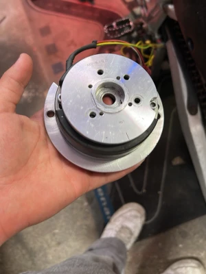 Rund metallisk maskindel med kablar - Säljer en rund maskindel i metall med flera hål och anslutna kablar. Delens yta är silverfärgad och har en svart ring runt mitten. Perfekt för dig som gillar att meka eller behöver reservdelar till maskiner eller elektronikprojekt.