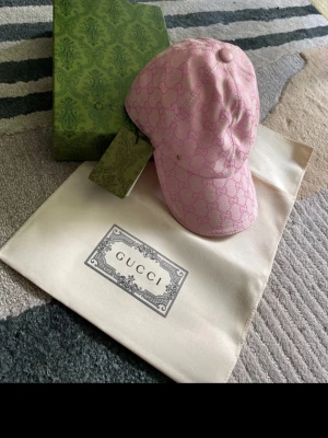 Rosa Gucci keps - Säljer en snygg rosa keps från Gucci med det klassiska GG-monogrammet över hela kepsen. Kepsen har böjd skärm och justerbar rem bak. Materialet känns lyxigt och kepsen kommer med originalpåse och tagg.
