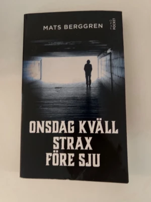 Onsdag kväll strax före sju pocket - En svart pocketbok av Mats Berggren med titeln 'Onsdag kväll strax före sju'. Omslaget visar en siluett i en tunnel med ljus i bakgrunden. Boken handlar om ungdomar i förorten och deras vardagliga utmaningar och relationer.