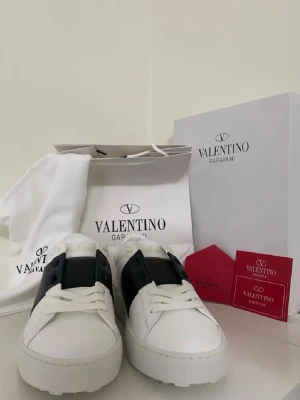 Valentino Garavani vita sneakers - Stilrena vita sneakers från Valentino Garavani med svart detalj på sidan. Skorna har klassisk låg profil, rund tå och är tillverkade i läder. Perfekta för dig som gillar exklusiv och modern design.