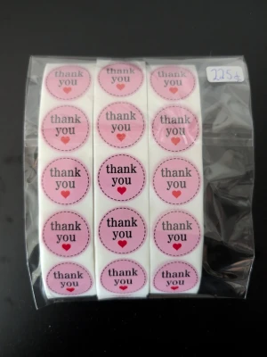 Rosa thank you-klistermärken 225 st - Ett paket med runda rosa klistermärken med texten 'thank you' och ett litet rött hjärta. Perfekta för att dekorera paket, brev eller presenter. Kommer i en genomskinlig plastförpackning och varje etikett har en söt design.
