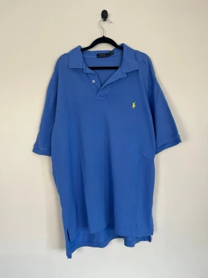Polo Ralph Lauren Pikétröja Blå Classic Fit Gul Logo Bomull Stl XL - • Storlek: XL • Färg: Blå • Passform: Classic Fit • Krage: 2-knappsstängning • Material: 100% bomull   Skick: Plagget är i väldigt fint skick med en mindre fläck på framsidan. Eventuella anmärkningar anges alltid tydligt i beskrivningen och visas på bilderna.  Nypris: Cirka 1 600 kr.  📦 Skickas snabbt och packas omsorgsfullt. 💬 Hör gärna av dig om du har frågor eller vill se fler bilder. 🤝 Samfrakt erbjuds vid köp av flera plagg – kika gärna in mina andra annonser!